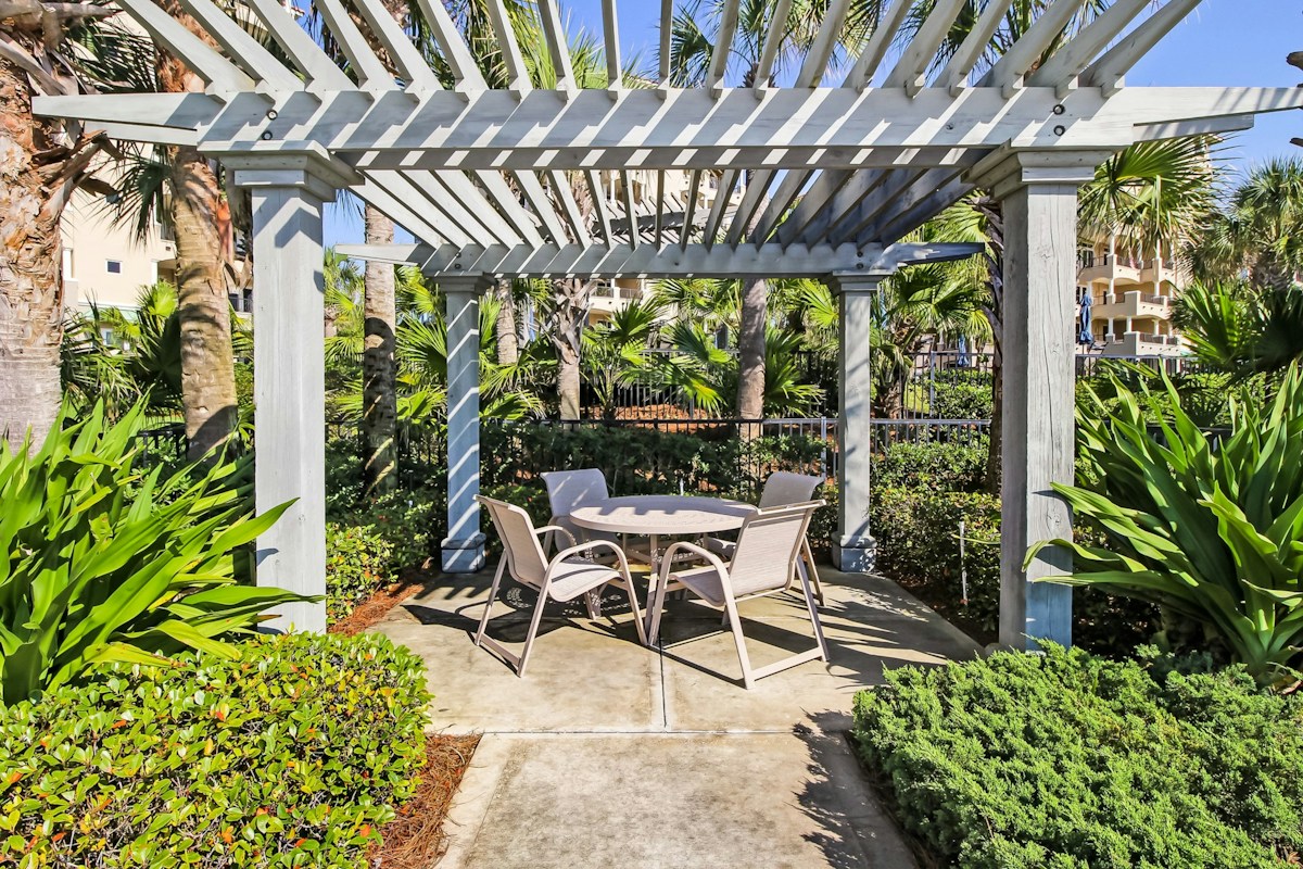 Garden dining area beneath a white pergola surrounded by tropical greenery